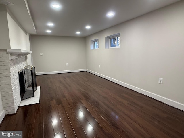 unfurnished living room with dark wood-style floors, recessed lighting, a brick fireplace, and baseboards