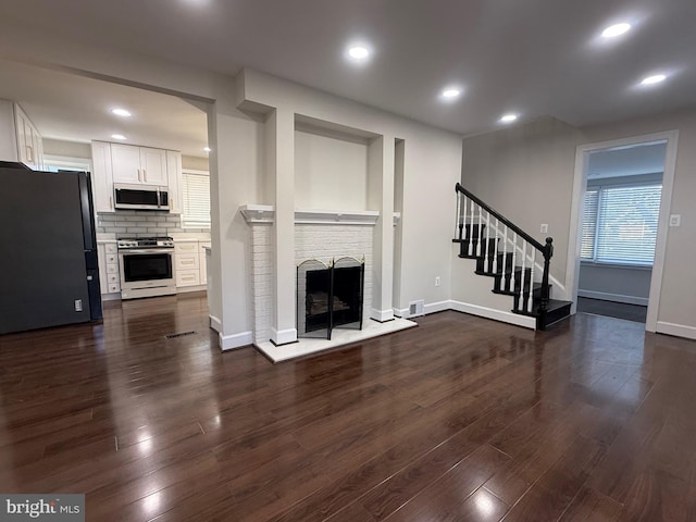 unfurnished living room with visible vents, dark wood-type flooring, stairs, recessed lighting, and a fireplace