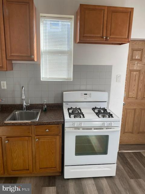 kitchen featuring brown cabinetry, dark wood-style flooring, white range with gas stovetop, and a sink