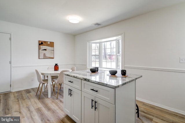 kitchen with a kitchen island, light stone countertops, visible vents, and light wood-type flooring