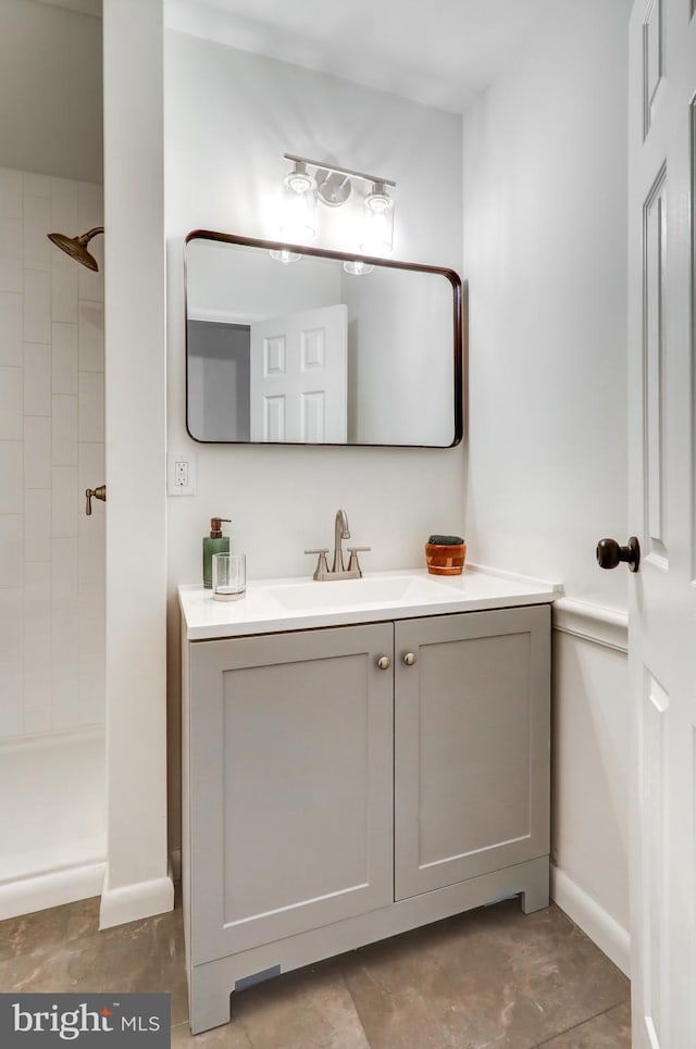 bathroom featuring baseboards, tiled shower, and vanity