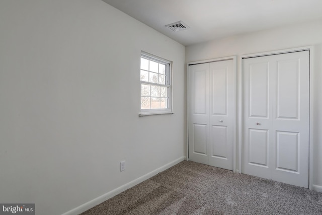 unfurnished bedroom featuring multiple closets, carpet, visible vents, and baseboards