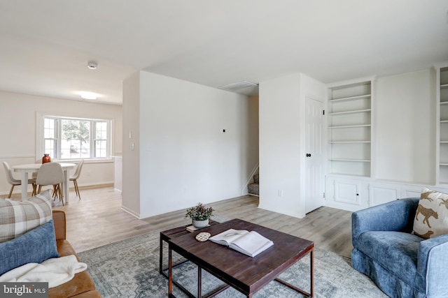 living area with stairs, built in shelves, and light wood finished floors