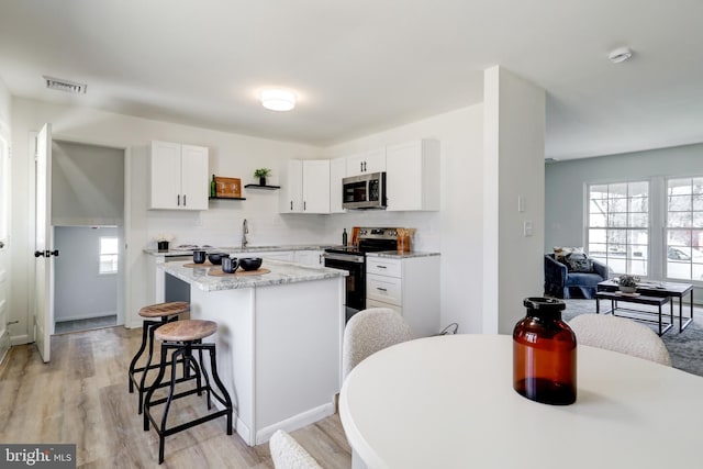 kitchen featuring visible vents, open shelves, appliances with stainless steel finishes, a kitchen bar, and a center island