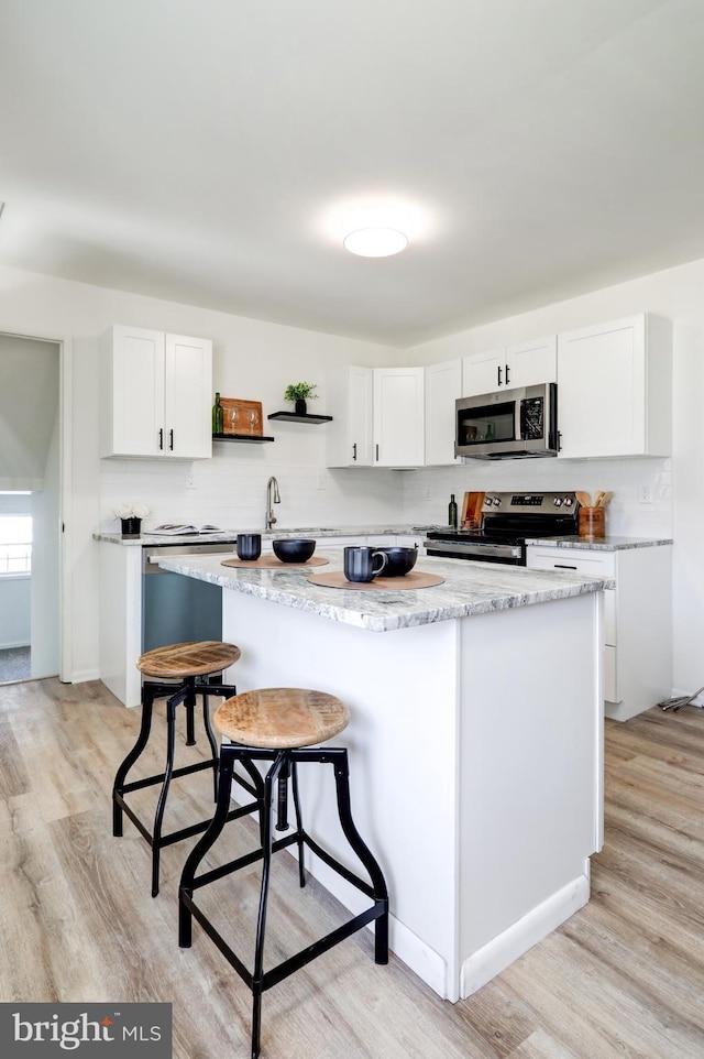 kitchen featuring white cabinets, stainless steel appliances, light wood-type flooring, and open shelves