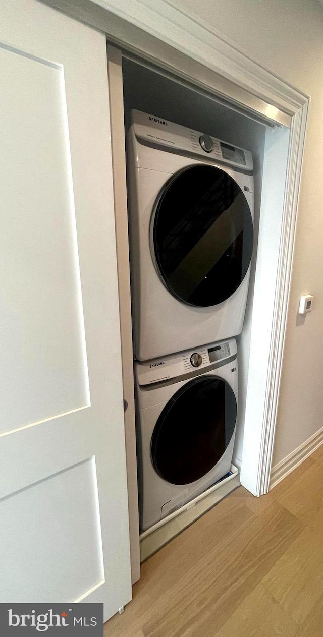 laundry area with baseboards, stacked washer and clothes dryer, laundry area, and light wood finished floors