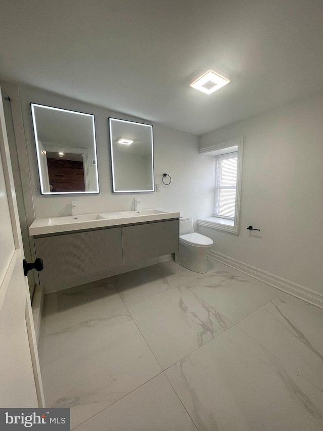 bathroom with baseboards, double vanity, a sink, toilet, and marble finish floor