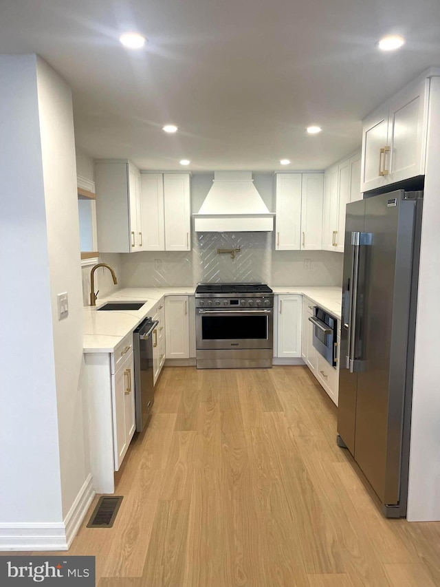 kitchen featuring light wood-style flooring, custom range hood, a sink, light countertops, and high end appliances