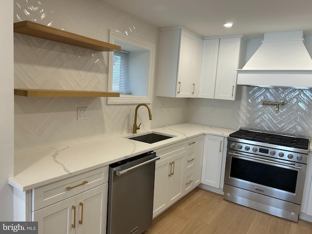 kitchen featuring light wood finished floors, a sink, stainless steel appliances, custom range hood, and white cabinets