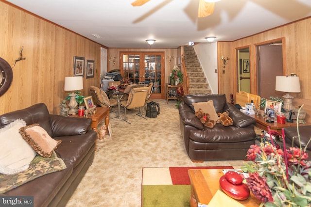 living area featuring carpet, ceiling fan, wood walls, stairs, and french doors