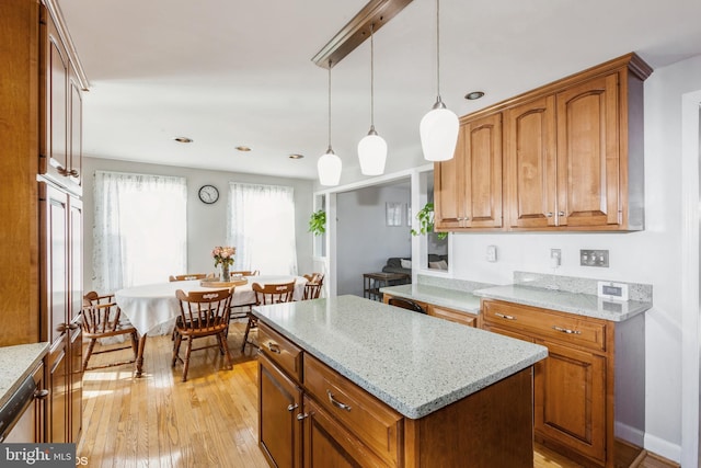 kitchen with light stone counters, brown cabinetry, light wood finished floors, hanging light fixtures, and a center island