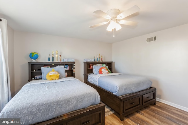 bedroom featuring a ceiling fan, wood finished floors, visible vents, and baseboards