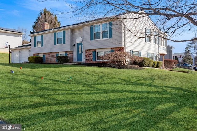 split foyer home with a front yard, a garage, brick siding, and a chimney