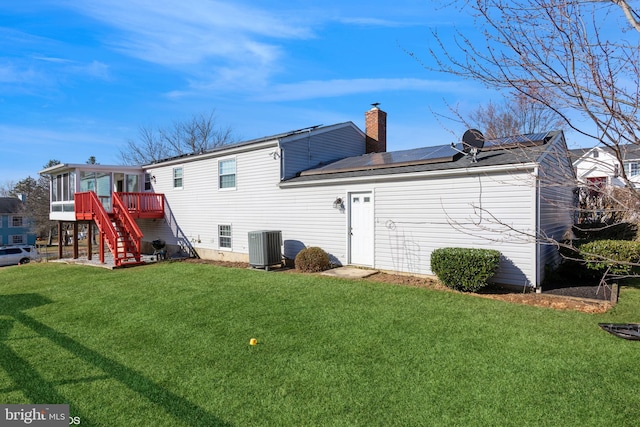 rear view of property with a sunroom, central AC, a chimney, a lawn, and roof mounted solar panels