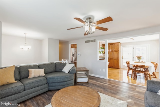 living room with visible vents, ceiling fan with notable chandelier, baseboards, and wood finished floors