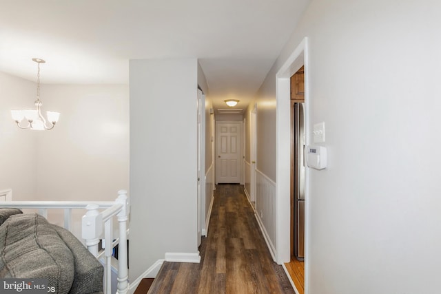 hall with an upstairs landing, baseboards, dark wood-type flooring, and an inviting chandelier