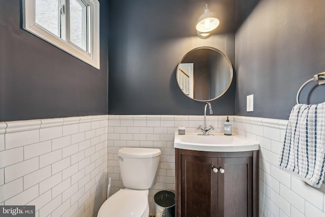 half bath with vanity, tile walls, toilet, and wainscoting