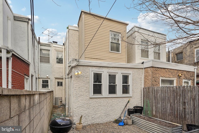 rear view of house featuring central AC unit, fence, and stucco siding