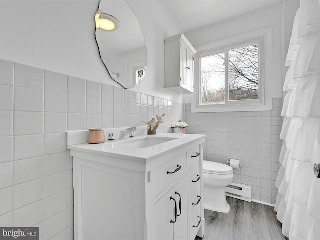 bathroom with toilet, wood finished floors, tile walls, a baseboard radiator, and vanity