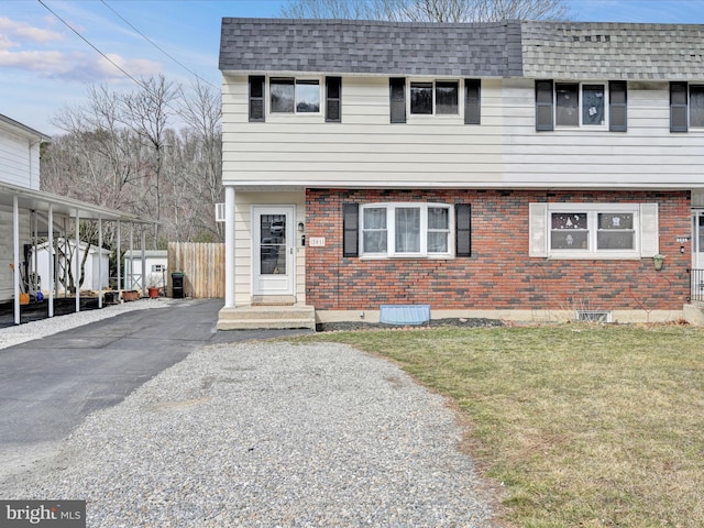 view of front facade featuring aphalt driveway, fence, roof with shingles, a front yard, and brick siding