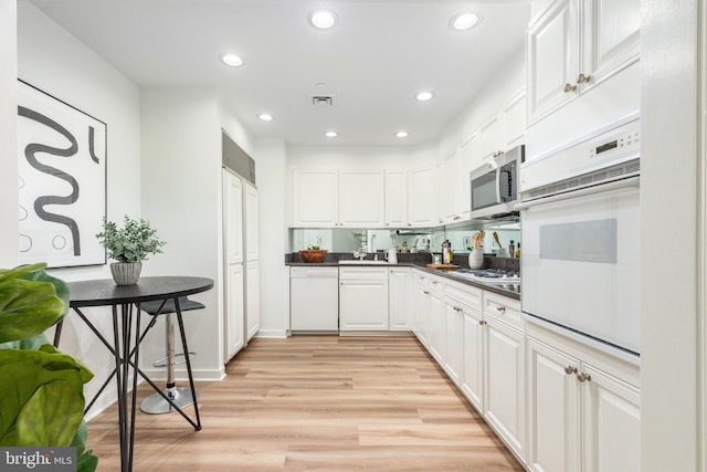 kitchen featuring dark countertops, recessed lighting, white appliances, light wood-style floors, and white cabinets