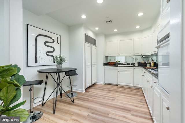 kitchen with dark countertops, visible vents, dishwasher, light wood-style flooring, and white cabinets