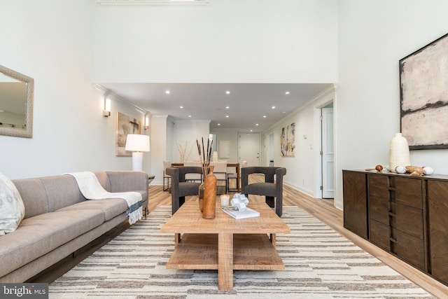 living area with crown molding, a high ceiling, recessed lighting, and light wood-style floors