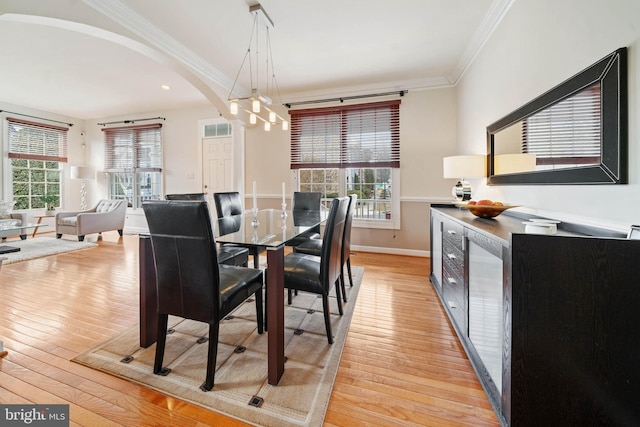 dining space featuring arched walkways, a healthy amount of sunlight, crown molding, and light wood-type flooring