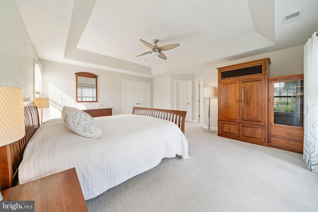 bedroom featuring a tray ceiling, light carpet, visible vents, and a ceiling fan