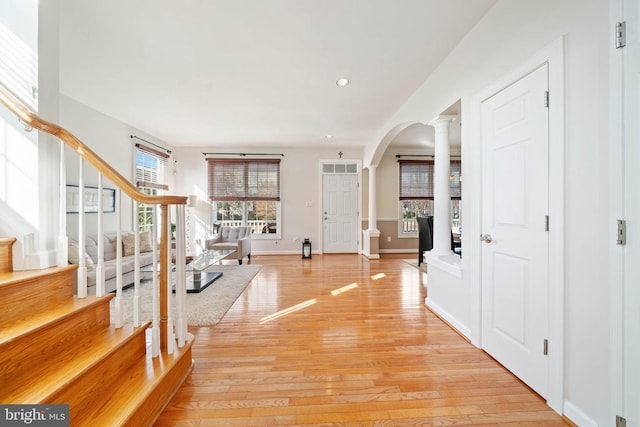 entrance foyer featuring stairway, baseboards, light wood finished floors, ornate columns, and arched walkways