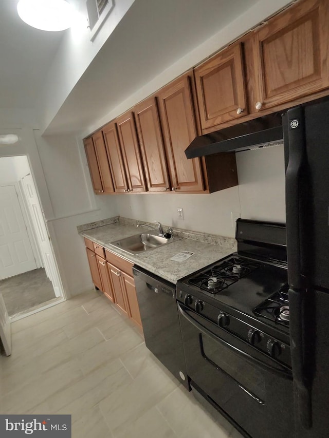 kitchen with under cabinet range hood, light countertops, brown cabinets, black appliances, and a sink