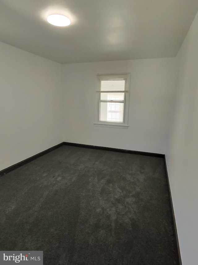 unfurnished room featuring baseboards and dark carpet