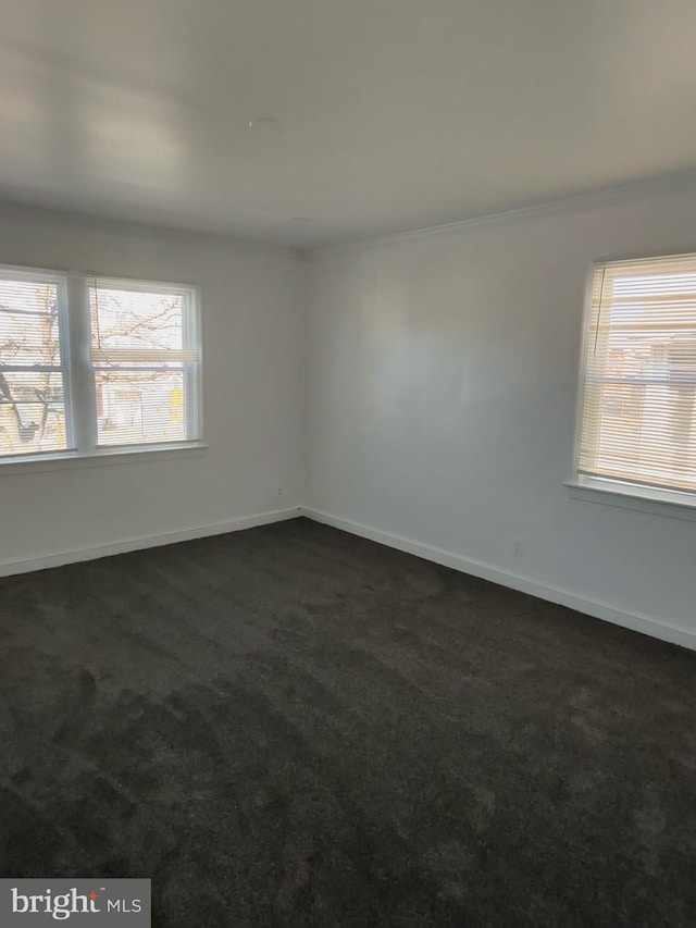 empty room featuring dark colored carpet, baseboards, and ornamental molding