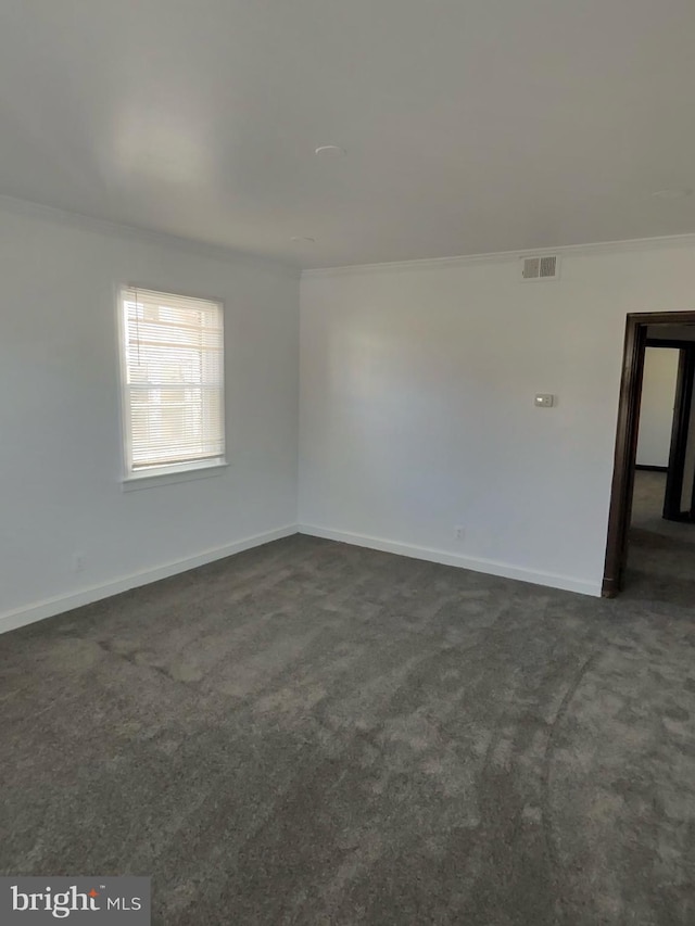 empty room featuring visible vents, baseboards, ornamental molding, and dark carpet