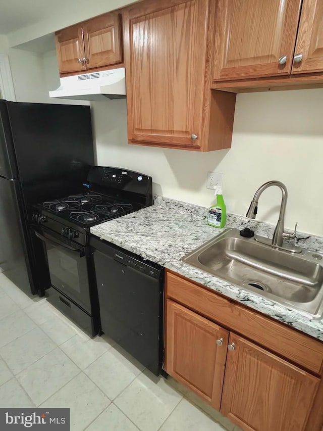 kitchen with under cabinet range hood, black appliances, brown cabinetry, and a sink