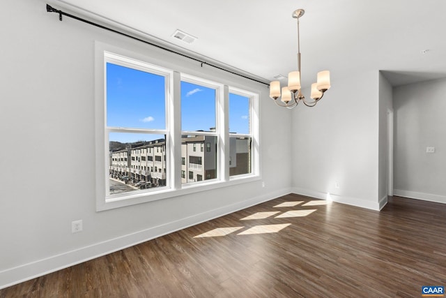 spare room featuring dark wood finished floors, a notable chandelier, a healthy amount of sunlight, and baseboards