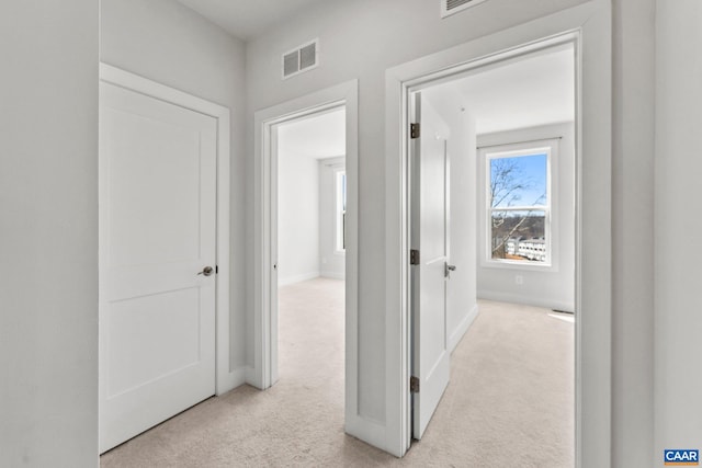 hallway with baseboards, visible vents, and light carpet