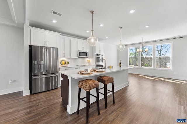 kitchen featuring dark wood-style floors, visible vents, a kitchen island with sink, decorative backsplash, and appliances with stainless steel finishes