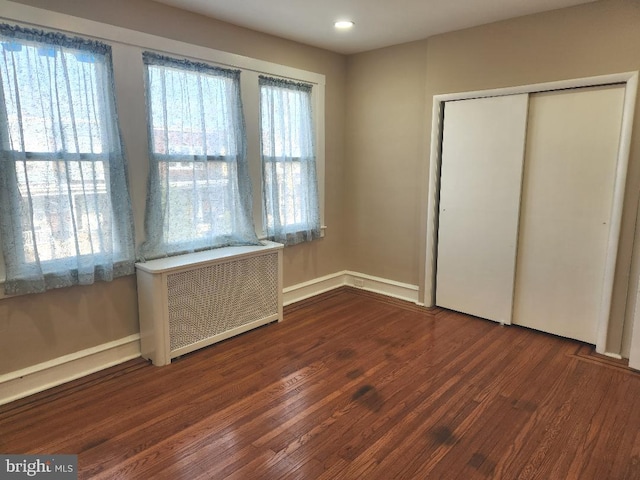 unfurnished bedroom with a closet, baseboards, wood finished floors, and radiator heating unit