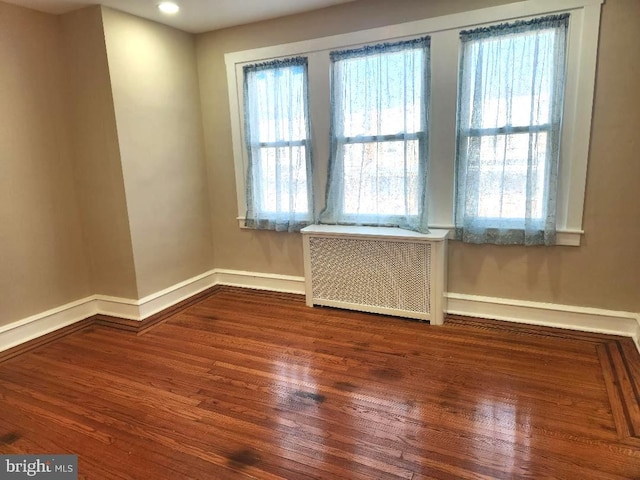 unfurnished room featuring baseboards, wood finished floors, and radiator heating unit