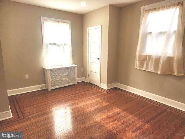 empty room with baseboards, wood finished floors, and radiator heating unit