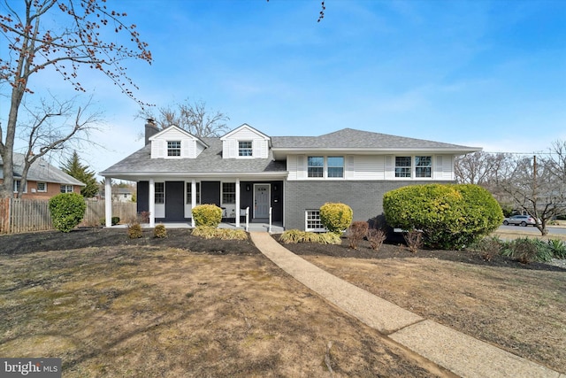 tri-level home featuring fence, roof with shingles, a porch, a chimney, and brick siding