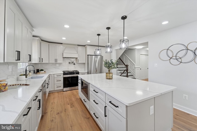 kitchen with a sink, custom range hood, light wood-style floors, appliances with stainless steel finishes, and backsplash