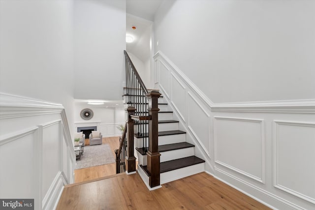 stairway with a decorative wall, a fireplace, and wood finished floors