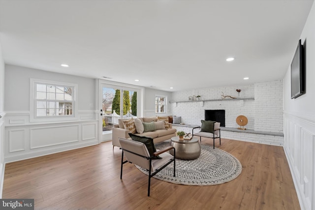 living room featuring a brick fireplace, a decorative wall, wood finished floors, and brick wall