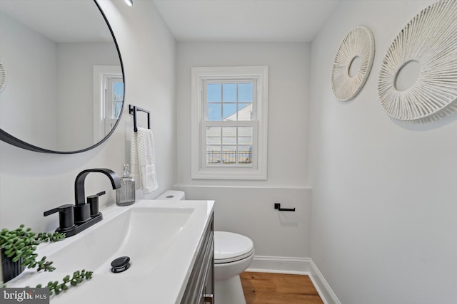 half bath featuring baseboards, toilet, wood finished floors, and vanity