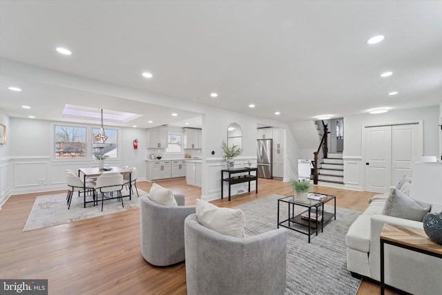 living area featuring stairway, recessed lighting, a decorative wall, and light wood-style floors