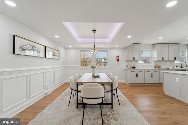 dining area with visible vents, recessed lighting, light wood-style floors, wainscoting, and a raised ceiling