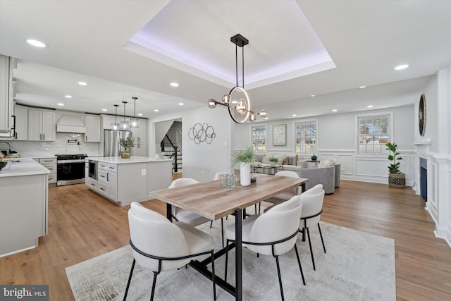 dining space with stairway, a tray ceiling, recessed lighting, light wood-style floors, and a decorative wall