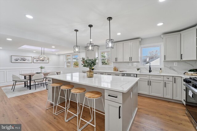 kitchen with light wood finished floors, a wainscoted wall, a kitchen island, and a sink